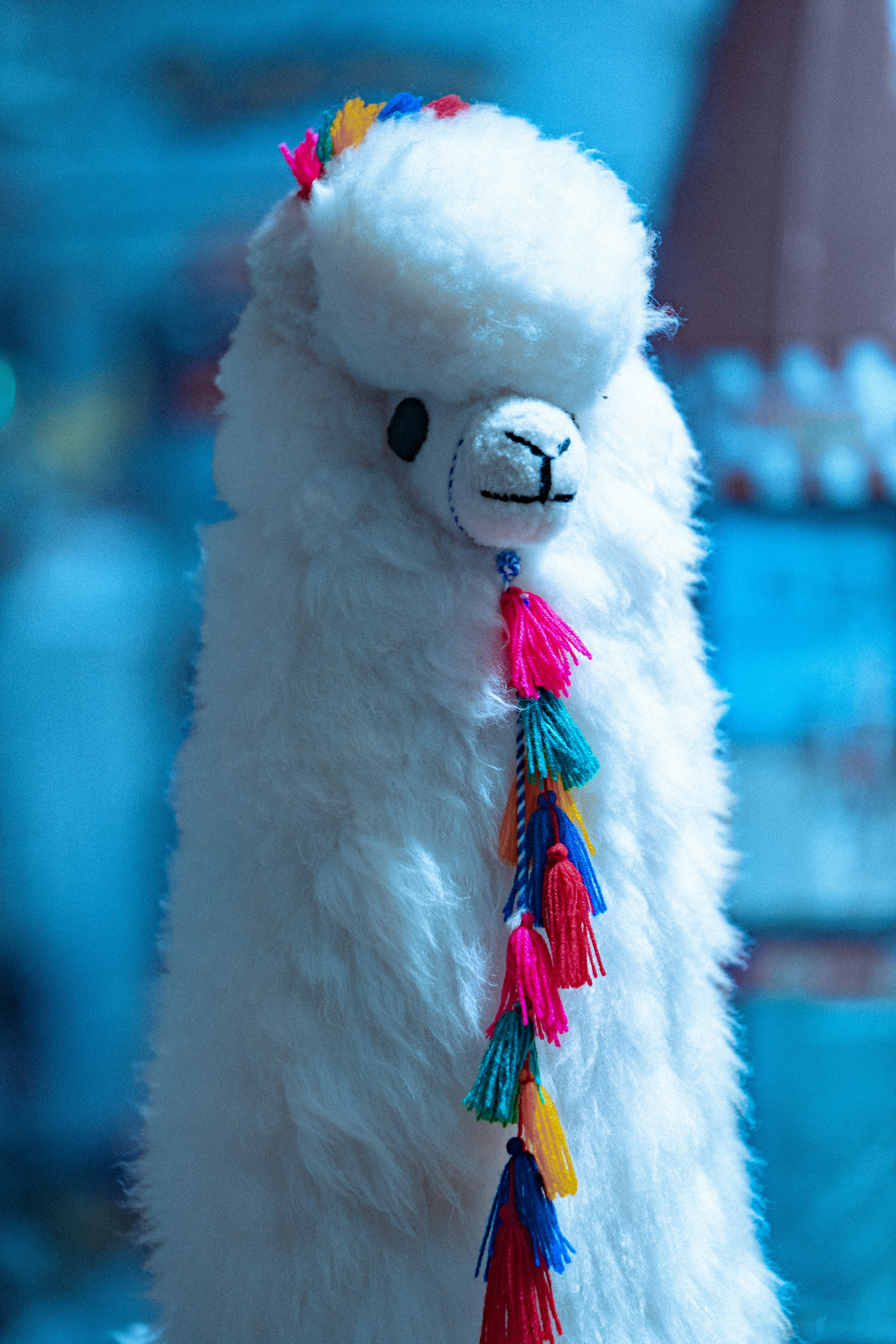 a white stuffed llama with a colorful tassel around its neck