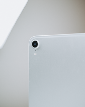 A close-up view of the back corner of a sleek electronic device, focusing on its camera lens and a small microphone hole. The device has a minimalistic and modern design with a metallic finish.