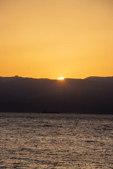 A serene sunset over calm ocean waters with a lone ship silhouette in the distance.