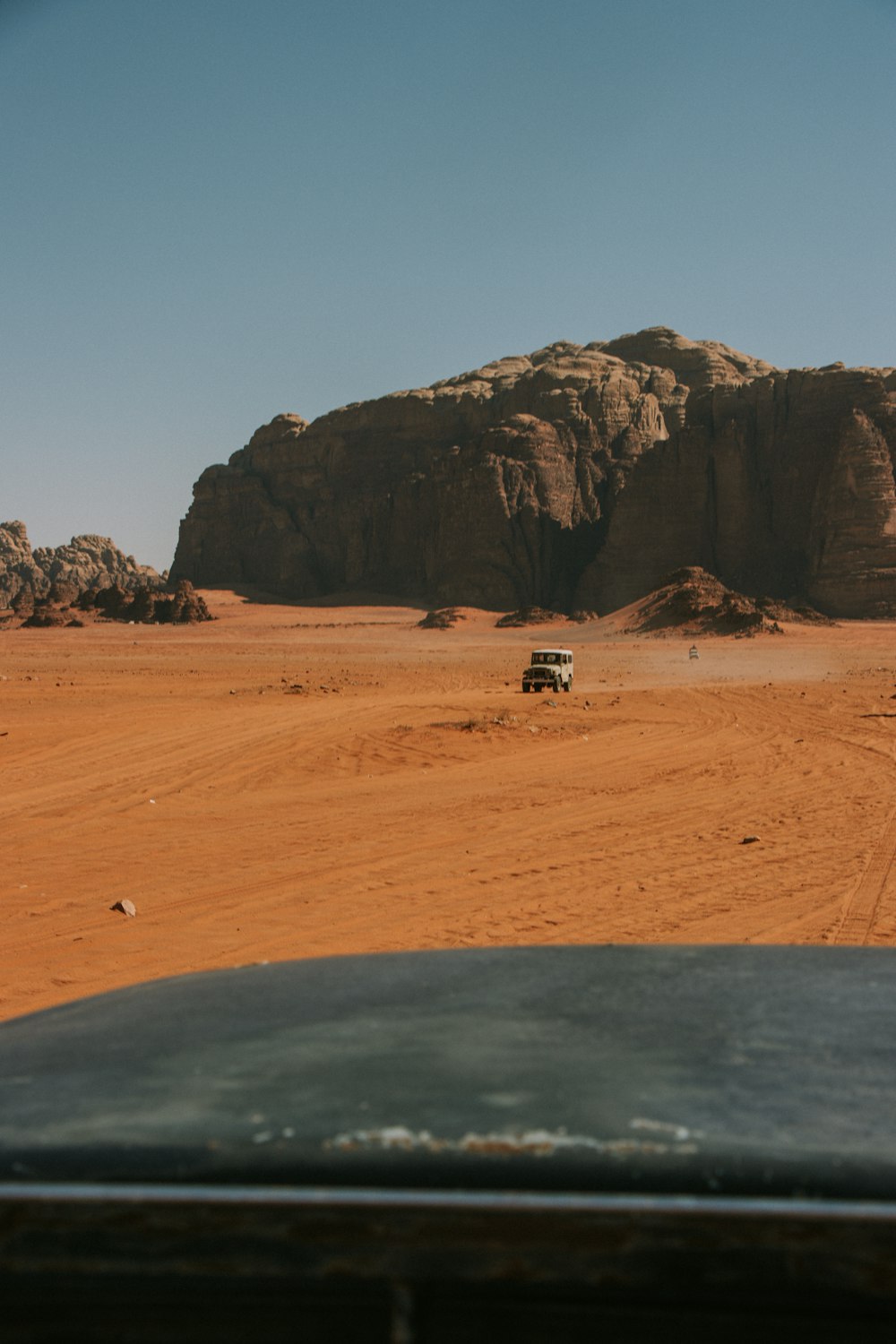 a car driving through a desert with a rock formation in the background