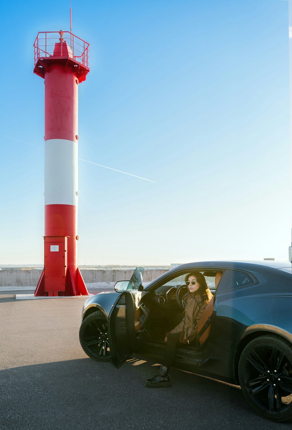a woman sitting in a car next to a red and white lighthouse