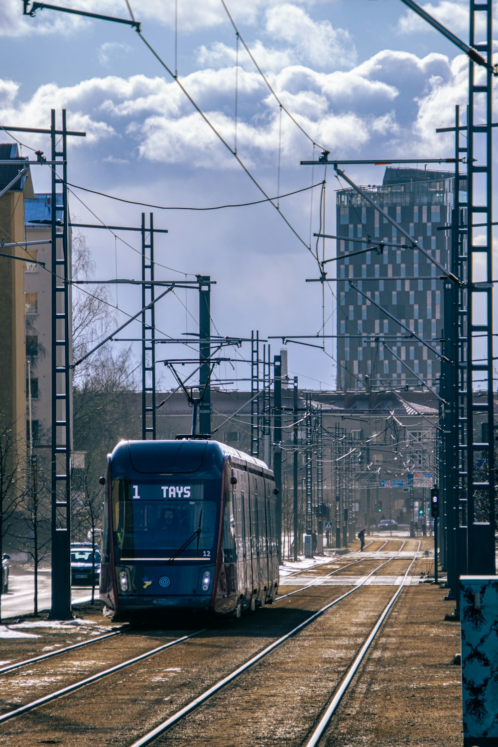 a blue train traveling down train tracks next to tall buildings