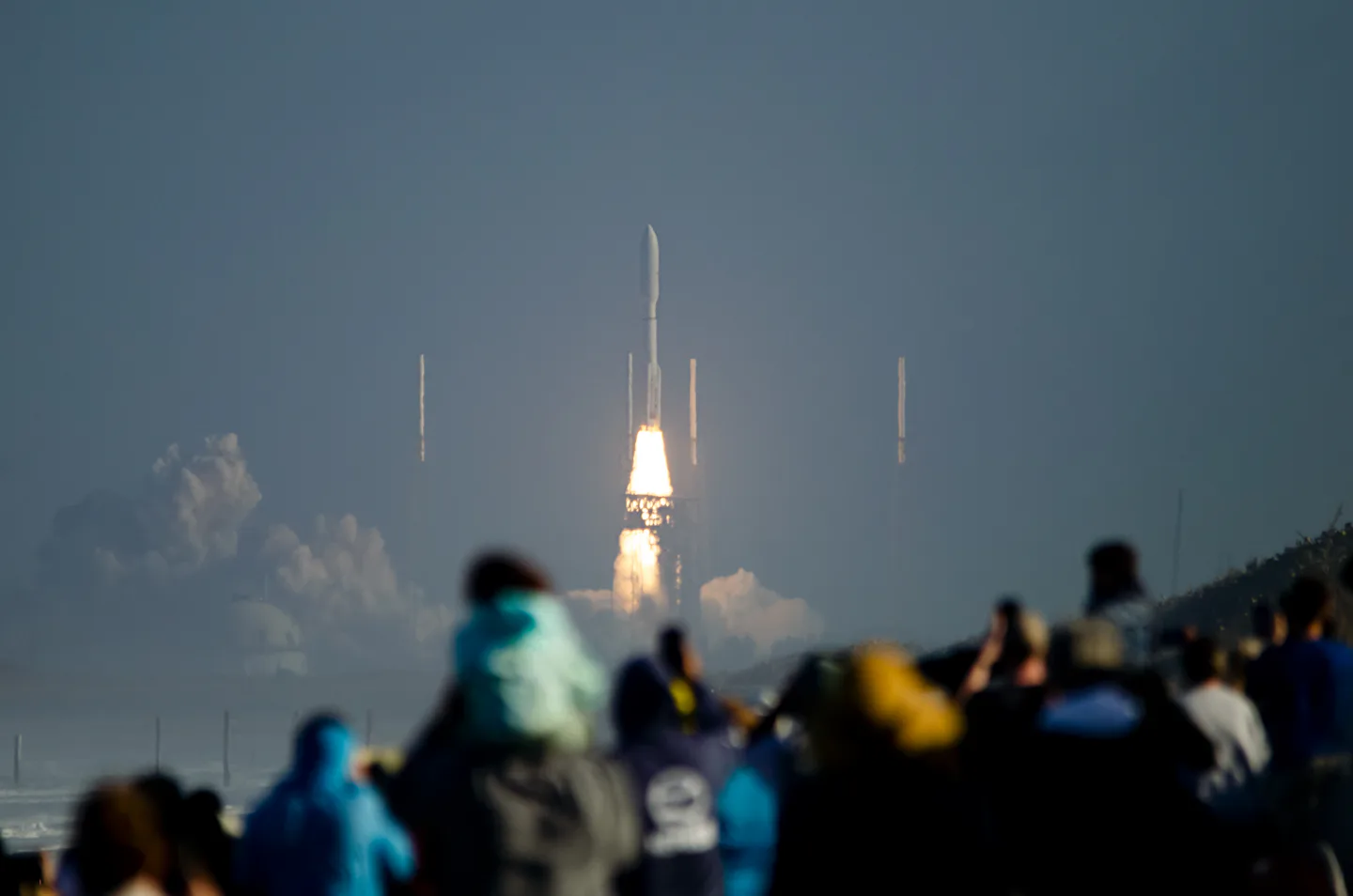 A crowd watching a rocket launch from the shore