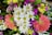 A vibrant bouquet featuring a mix of flowers including white daisies with yellow centers, bright pink and yellow blooms, and deep green foliage. The arrangement is lush and colorful, conveying a sense of freshness and vitality.