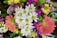 A vibrant bouquet featuring a mix of flowers including white daisies with yellow centers, bright pink and yellow blooms, and deep green foliage. The arrangement is lush and colorful, conveying a sense of freshness and vitality.
