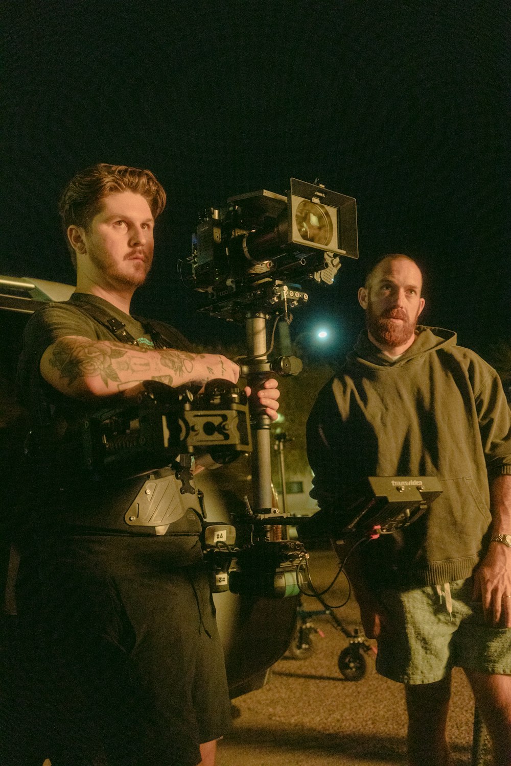 two men standing next to each other in front of a camera