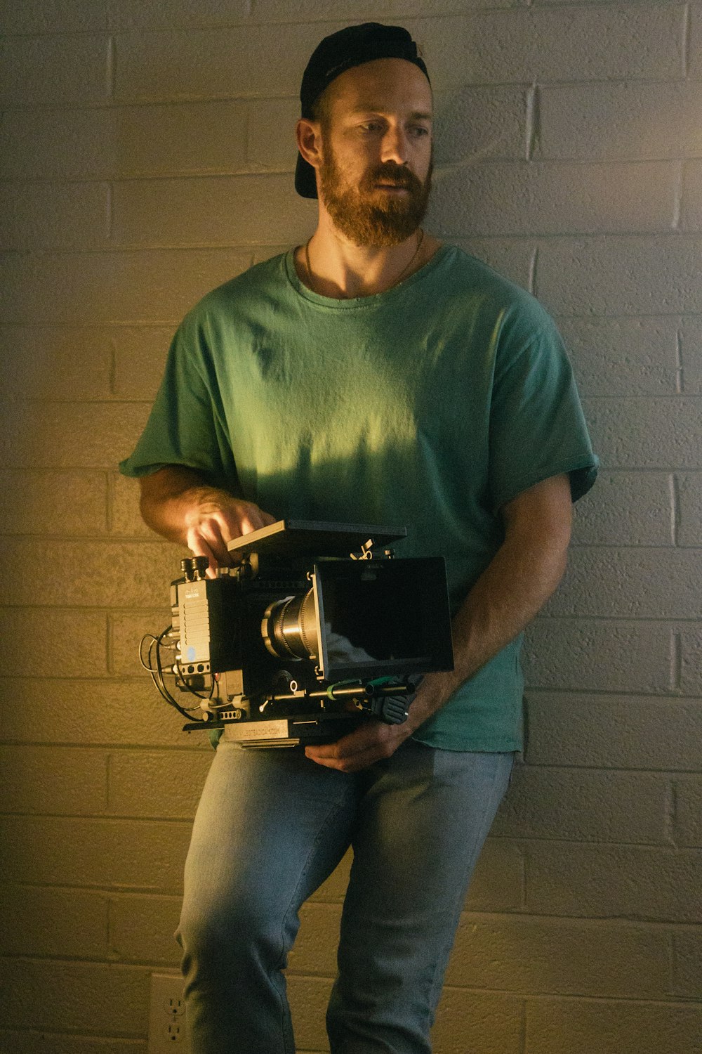a man holding a camera in front of a brick wall