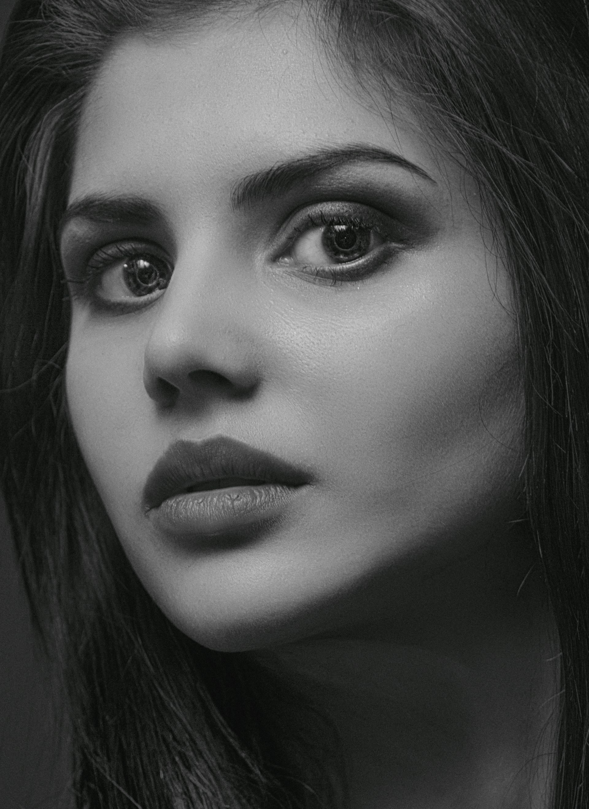 A striking black-and-white portrait of a woman, her eyes telling a powerful story against a smooth charcoal grey background.