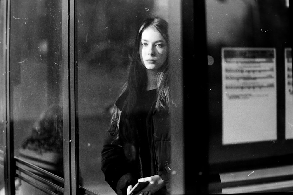 a black and white photo of a woman looking out a window