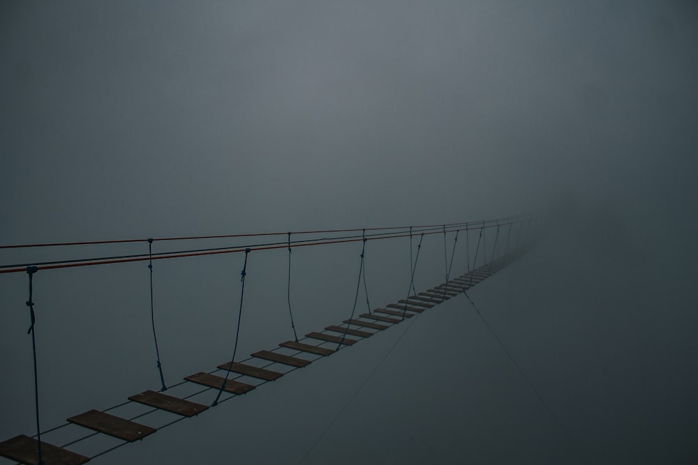 a rope bridge in the middle of a foggy sky