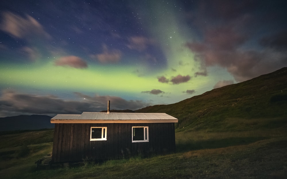 a small cabin in a field with the aurora behind it