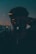 A reflective surface displays an ambiguous and abstract scene, where the silhouette of a person appears in front of a window. The background hints at a seascape with a skyline and a setting or rising sun. The dim lighting and blurred effect add to the mystery of the scene.