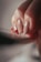A close-up of a person's hand focusing on their polished nails. The nails are painted in a glossy, neutral color with one nail featuring a hint of glitter. The lighting creates soft shadows, enhancing the textures of the fingers and nails.