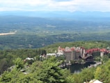 An expansive view of a scenic landscape featuring a large, historic resort complex nestled among lush greenery, with mountains in the background and a serene body of water in the foreground.