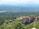 An expansive view of a scenic landscape featuring a large, historic resort complex nestled among lush greenery, with mountains in the background and a serene body of water in the foreground.