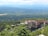 An expansive view of a scenic landscape featuring a large, historic resort complex nestled among lush greenery, with mountains in the background and a serene body of water in the foreground.