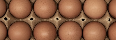 A close-up view of a dozen brown eggs arranged in a carton, showcasing their smooth, speckled surfaces nestled in a grid pattern.