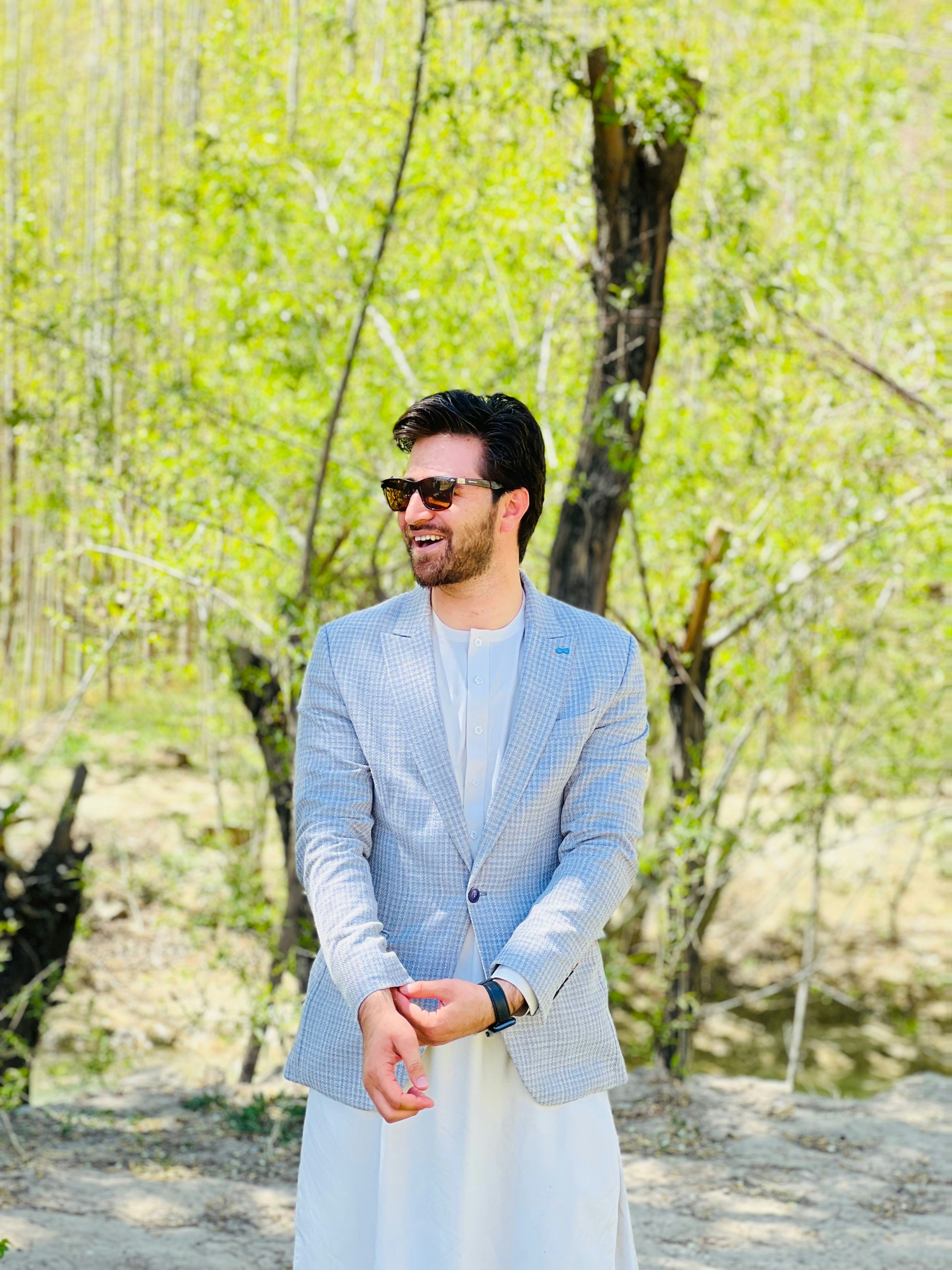 Man smiling outdoors in casual setting with greenery background
