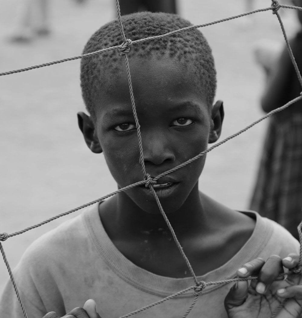 a young boy standing behind a wire fence
