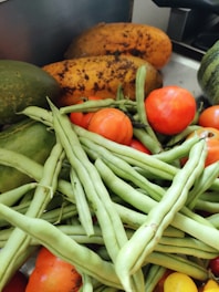 A collection of fresh vegetables including ripe tomatoes, green beans, papayas, and cucumbers arranged together.