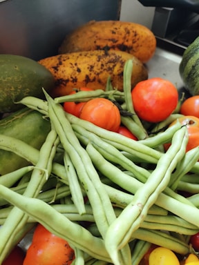 A collection of fresh vegetables including ripe tomatoes, green beans, papayas, and cucumbers arranged together.