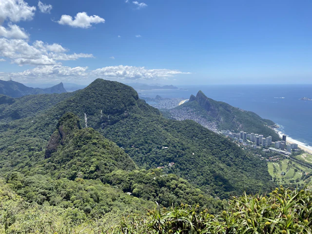 An aerial view from Pedra Bonita's launch point over forested peaks toward Rio's coastline and the Dois Irmãos twin peaks.