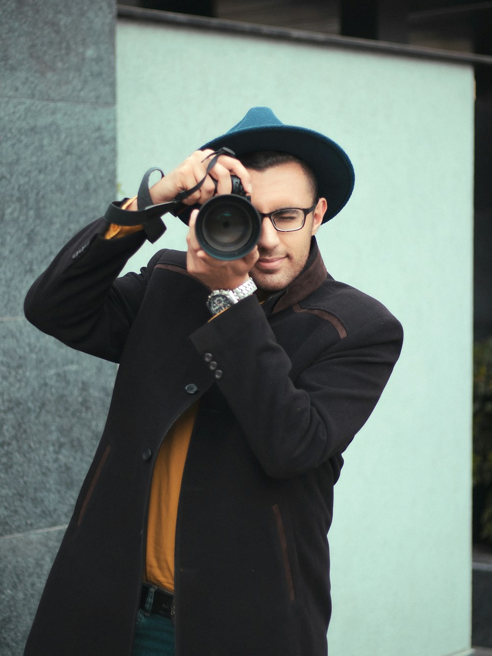 a man with a hat and glasses taking a picture with a camera