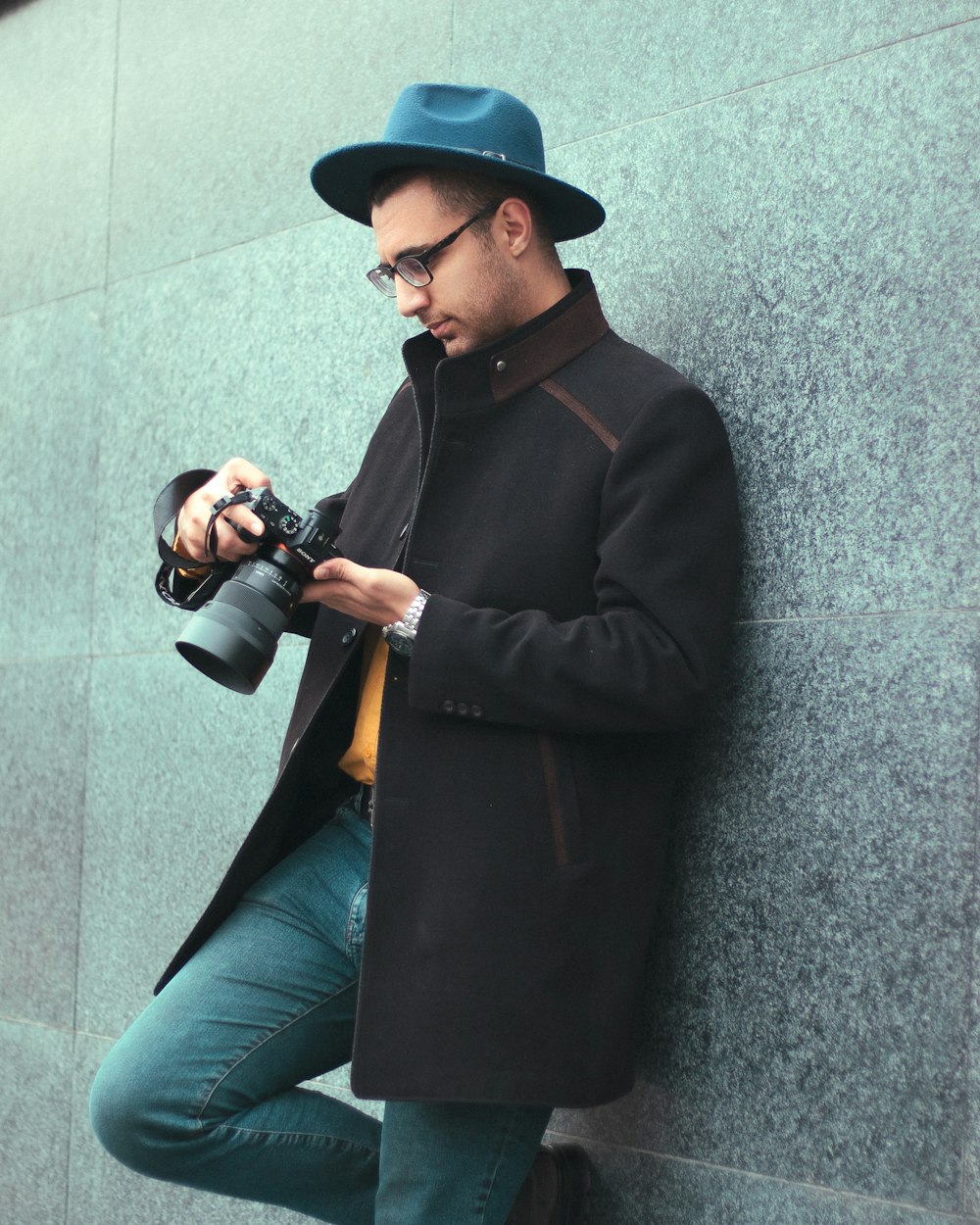 a man leaning against a wall holding a camera