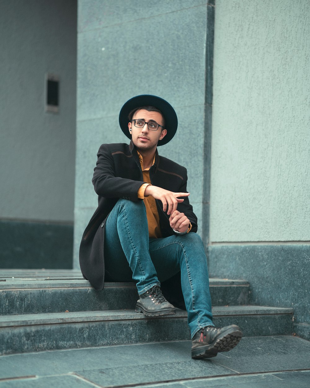 a man with a hat and glasses sitting on steps