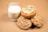 A small stack of assorted cookies, including one topped with colorful cereal and cream, is placed adjacent to a clear glass filled with milk. The background is a light brown surface that complements the warm hues of the cookies.