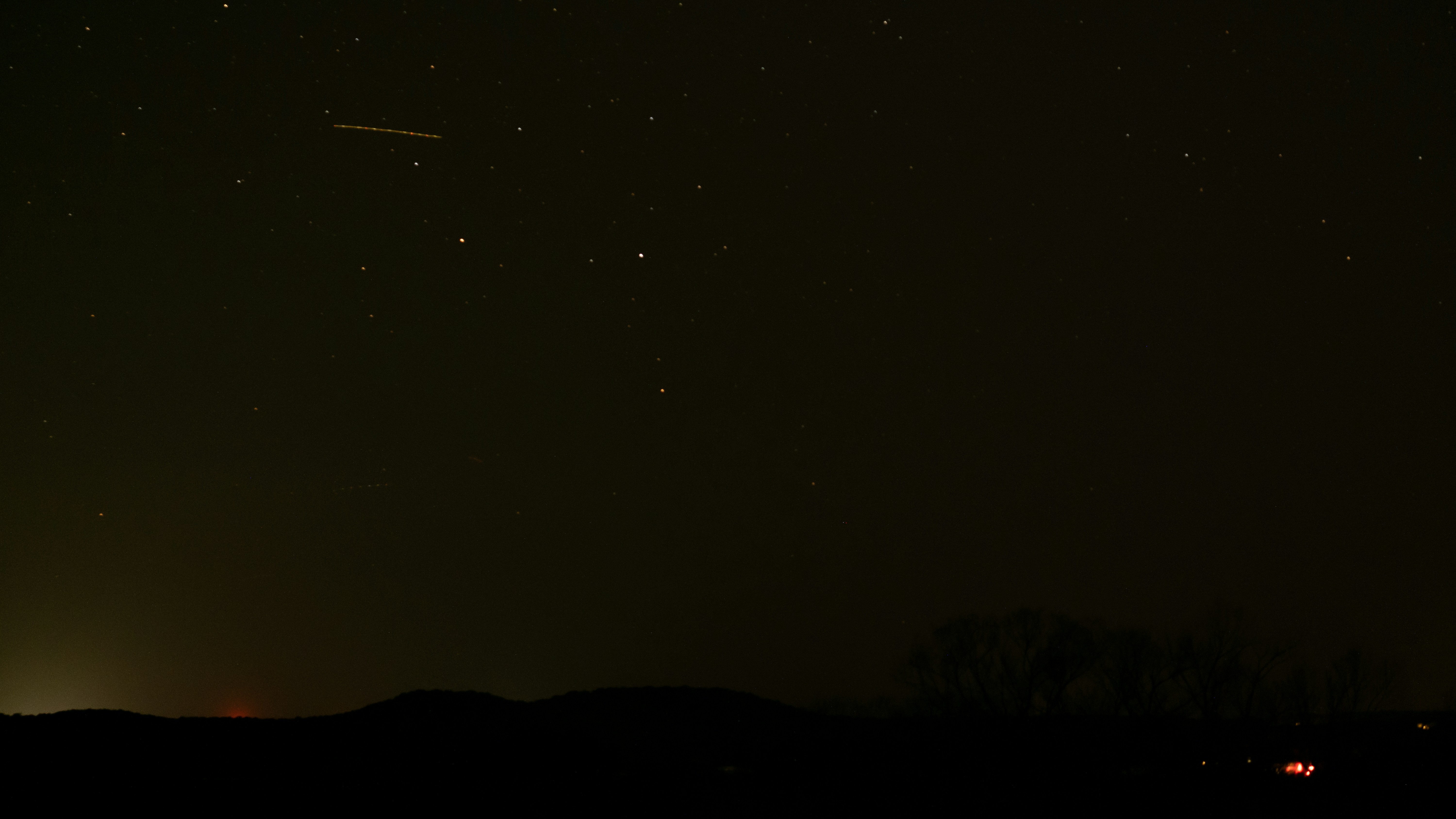 a night sky with stars and a plane in the distance