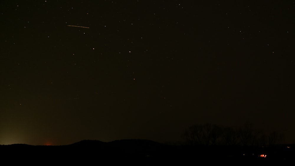 a night sky with stars and a plane in the distance