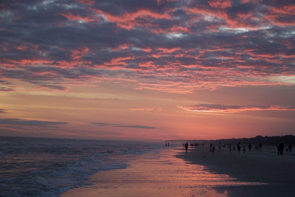 a group of people walking along a beach at sunset