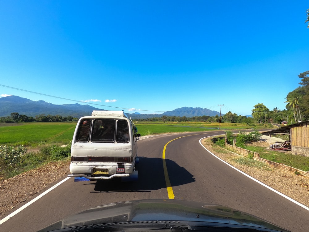 a van driving down a road next to a lush green field