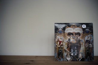 An album cover featuring intricate and detailed artwork with an ornate, carnival-themed frame. The eyes at the top draw the viewer's attention, surrounded by various figures and surreal elements.