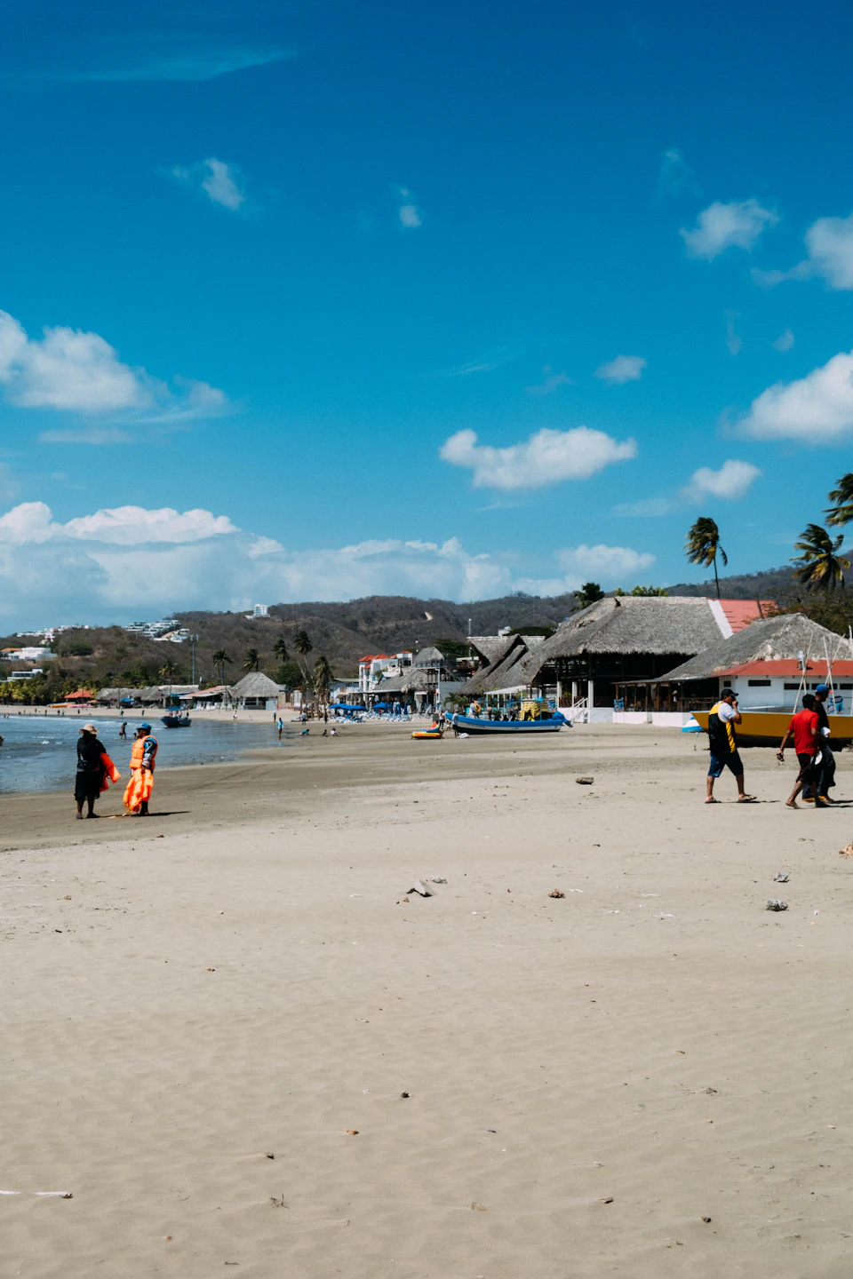 Group of people walking along serene sandy beach with clear blue sky and distant buildings