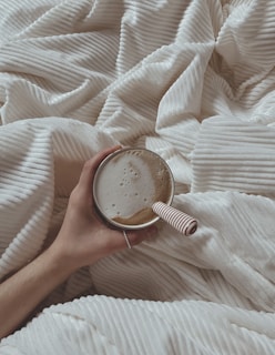a person holding a cup of coffee on a bed
