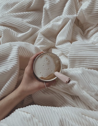 a person holding a cup of coffee on a bed