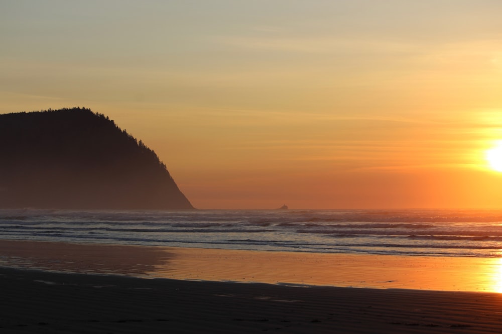 the sun is setting over a beach with a mountain in the background