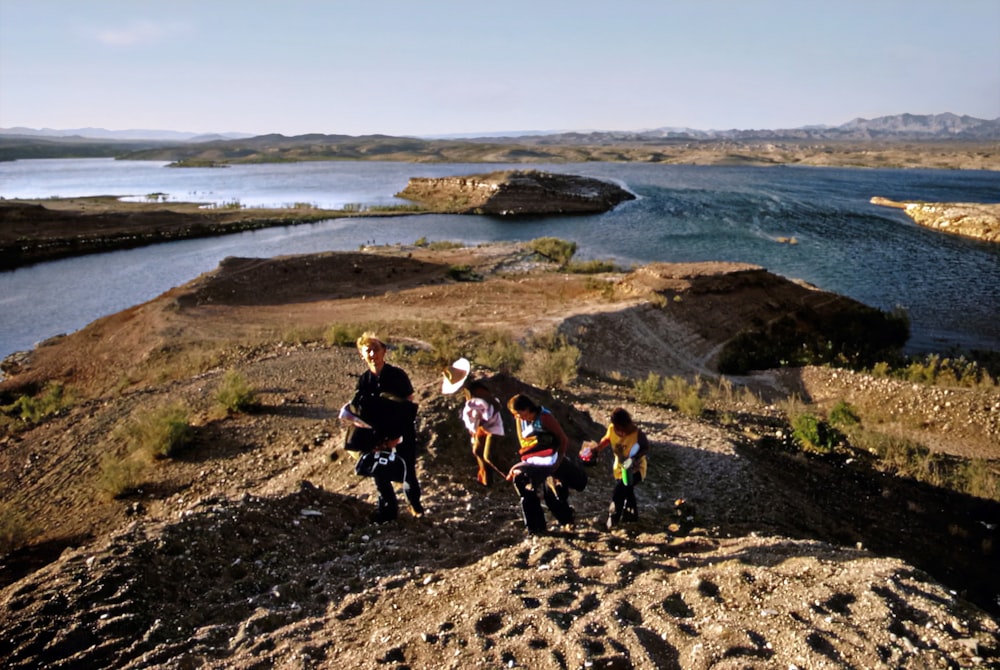 a group of people walking up a hill next to a lake