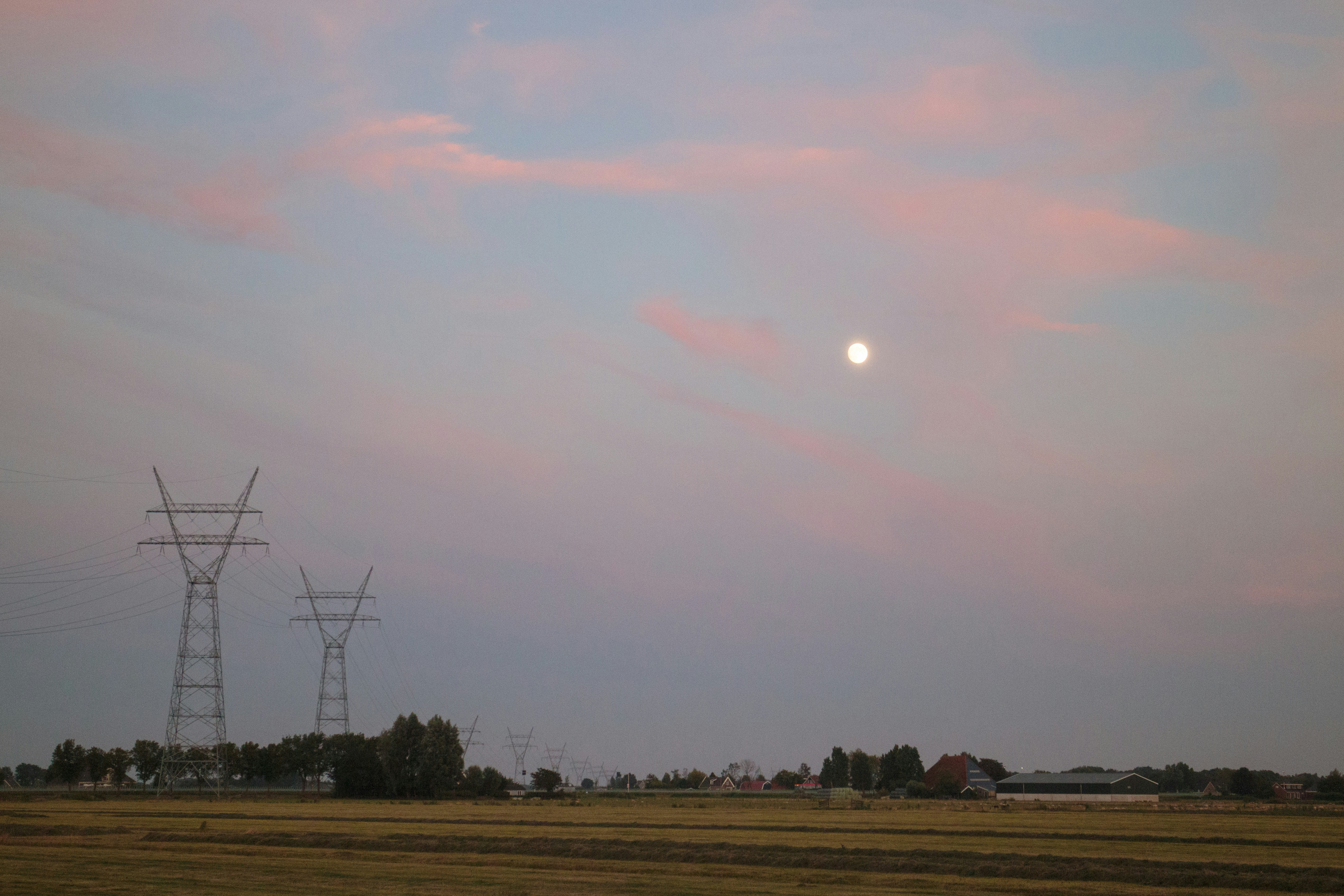 Die Sonne geht über einem Feld mit Stromleitungen unter