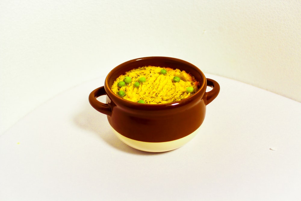 a brown and white bowl filled with food on top of a table