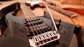 Three electric guitars are closely placed together, with a focus on the strings and bridge of the foremost black guitar. Various parts such as the neck, pickups, and volume knobs are visible, creating a detailed view of their construction.