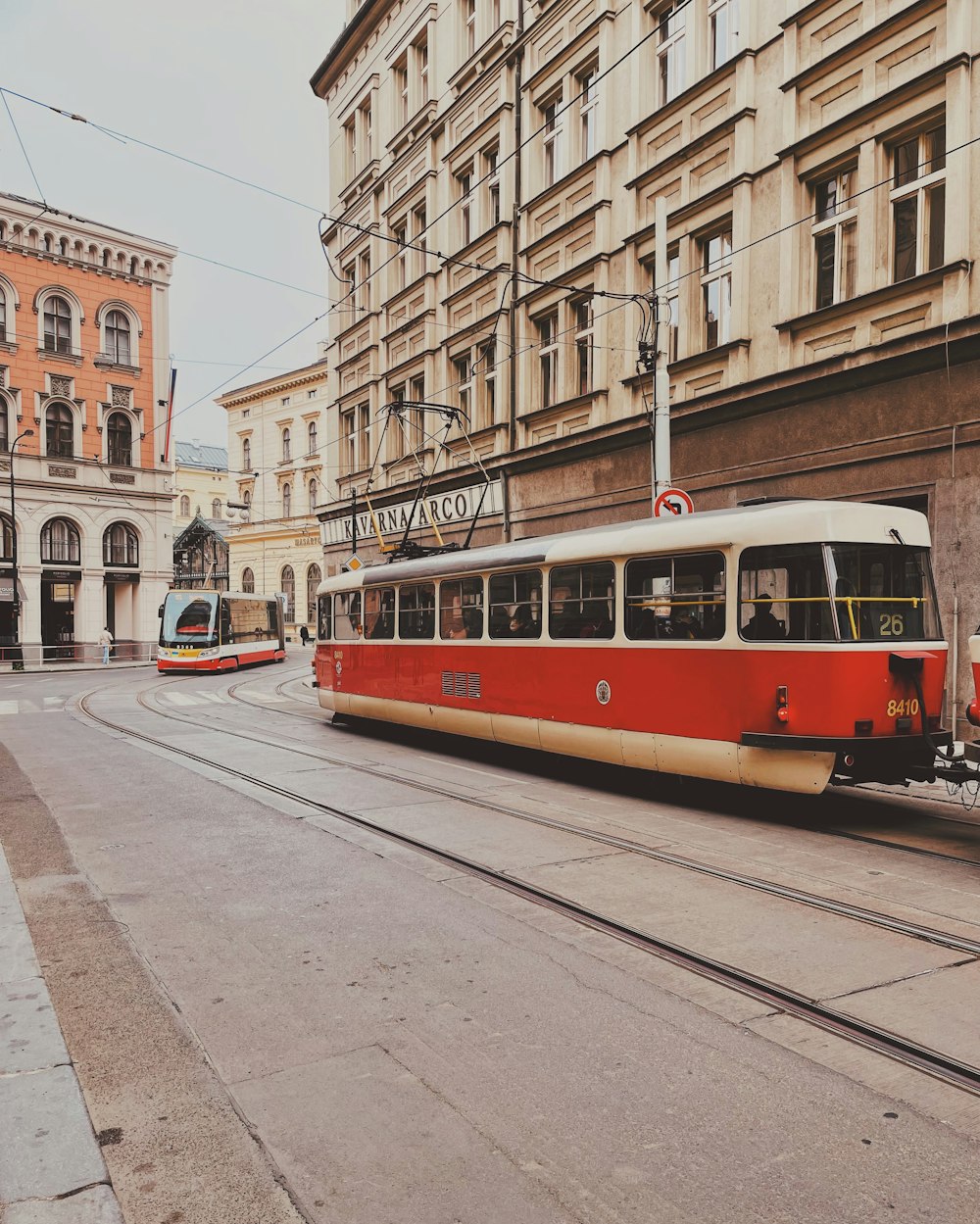 a red and white train traveling down a street next to tall buildings