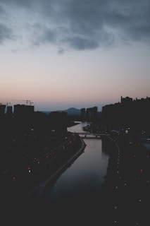 A serene city skyline at dawn with soft light illuminating the buildings and a winding river in the foreground.