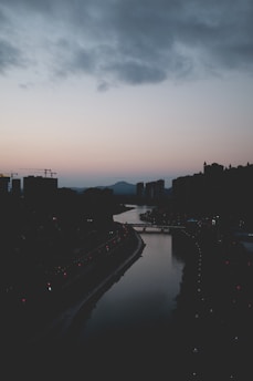 A serene city skyline at dawn with soft light illuminating the buildings and a winding river in the foreground.