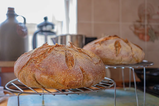 Close-up of rustic sourdough loaves cooling on a wooden rack beside the glowing oven.