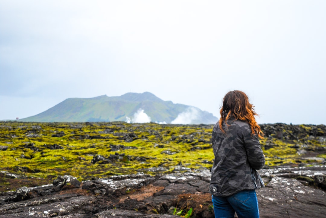 a woman standing on top of a lush green field, A girl looking over Icelandic landscape.