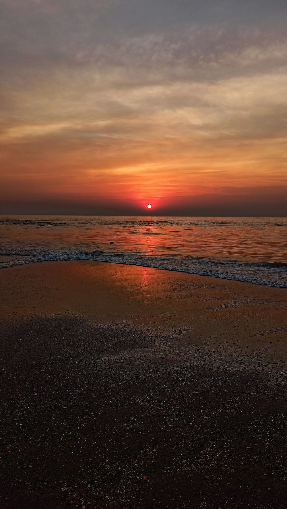 the sun is setting over the water on the beach