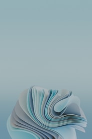 Delicate layers of folded paper-like material form a complex structure with soft curves and flowing lines. The composition is primarily in shades of blue and cyan, creating a sense of depth and motion.